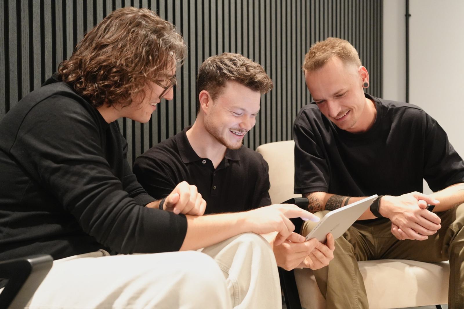 Peter, Patrick und Stefan von nonoise.digital sitzen lachend nebeneinander und schauen gemeinsam auf ein Tablet